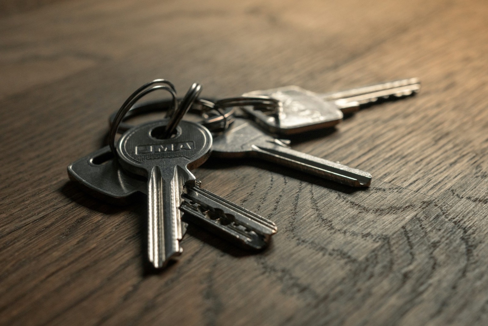 A set of house keys on a fob lying on a dark oak table in low, quiet interior light.