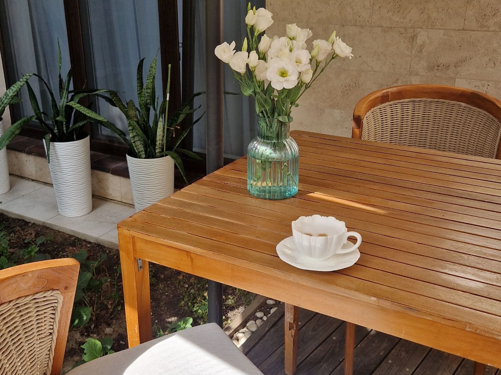 Two coffees and an open folder of statements on an outdoor table, with a quiet suburban garden beyond.