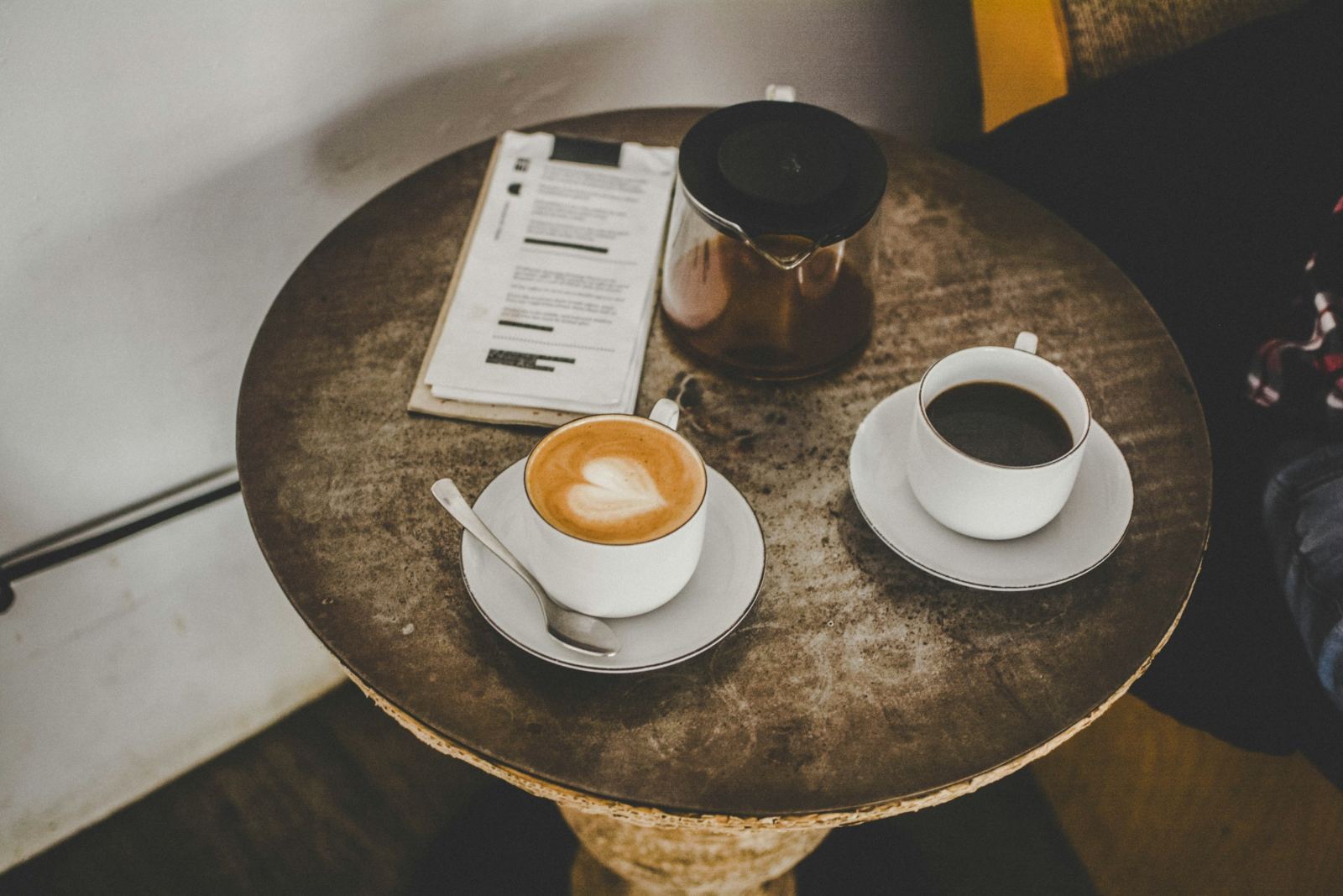 A single sheet of paper and two takeaway coffees on a bench in morning light.