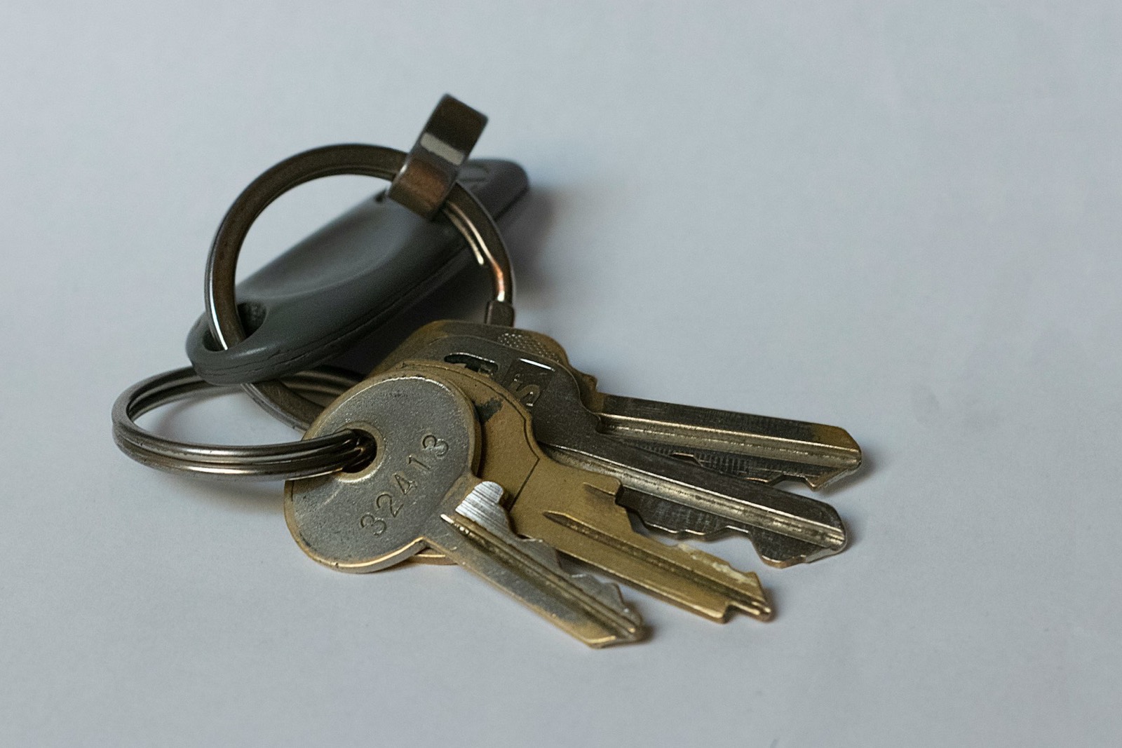 A set of house keys on a plain, pale grey surface in flat, even, cool light.